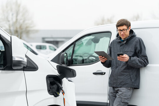 Fleet manager with digital tablet and smartphone supervising rows of white electric delivery vans