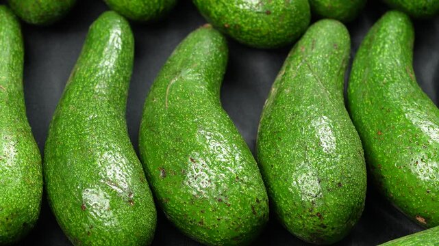 Macro close up of raw organic long green avocados on dark background.