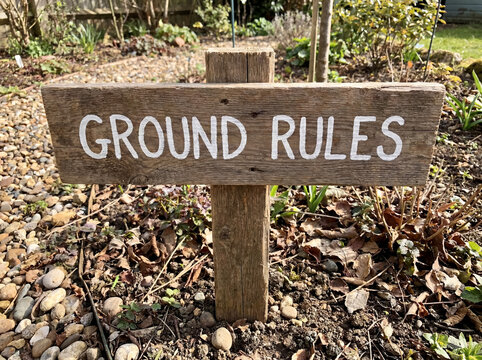 Ground rules sign made from weathered wood board with white paint lettering, offering guidance in a garden setting