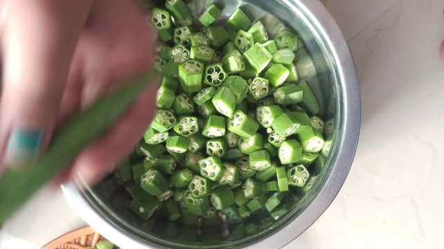 Slicing Fresh Green Okra into a Steel Bowl with a Knife, Close-up