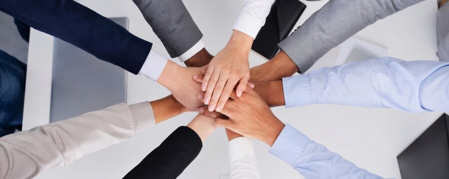Multiple hands of diverse individuals join together in a circle from a top-down perspective, symbolizing unity and strong teamwork.
