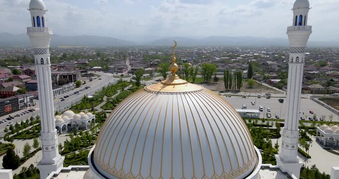 Epic aerial drone pull-away shot from the golden crescent spire on the main dome revealing the cityscape of Shali, Chechnya