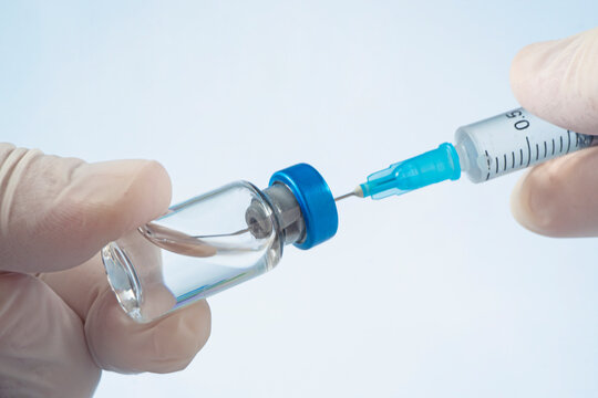 doctor draws medicine solution into syringe from vial on blue background. doctor hands and ampoule