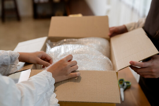 Small business owners packing fragile items with bubble wrap inside cardboard box during e-commerce shipping preparation and logistics fulfillment workflow