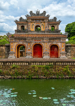 Hien Nhon Gate, Imperial City, Hue, Vietnam. Ornate traditional Vietnamese architecture with intricate details, vibrant colors, and a tranquil moat with lotus leaves under a cloudy sky