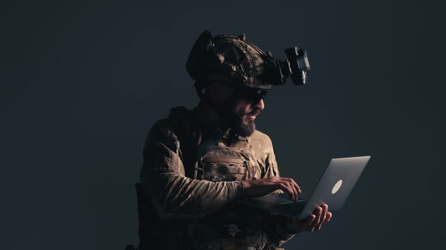 Fighter in contemporary combat gear interacts with a laptop, showcasing advanced technology integration in tactical operations against a dark background