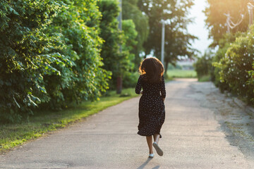 Back view of a woman in a black polka dot dress running down a suburban road. © Olga
