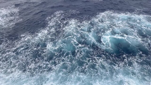 4K aerial side-view of a cruise ship cutting through dark Atlantic waters near Bermuda, sending turquoise waves and white foam cascading from the hull. Raw, unedited footage.