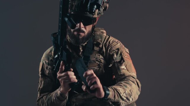 Service member in combat gear aims weapon forward, showcasing tactical readiness and focus in a controlled environment with neutral background lighting