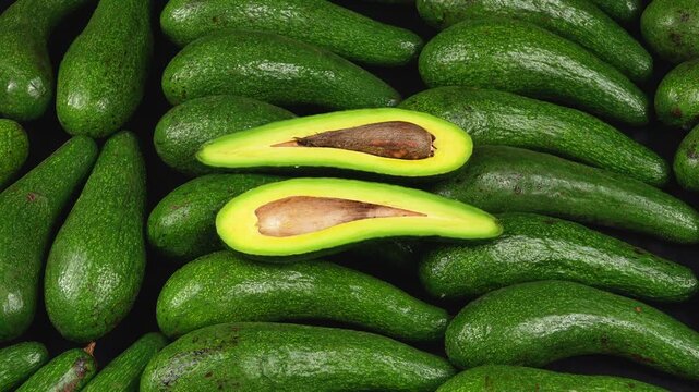 Sliced long avocado halves with brown seed on background of fresh whole green avocados.