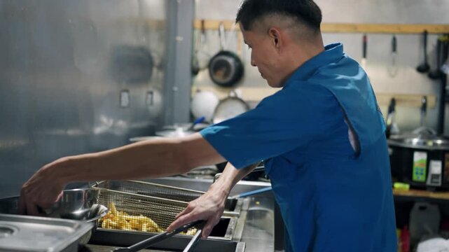 Professional cook preparing crispy french fries in a deep fryer. Man working in a commercial kitchen preparing a tasty fast food side dish