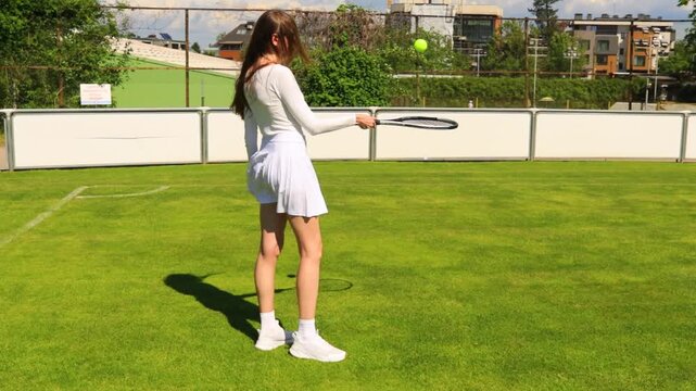 Young Woman Practicing Tennis Ball Juggling With Racket on Outdoor Clay Court, Female Athlete in White Sports Outfit Training Coordination and Ball Control During Sunny Day Match Practice, Handheld