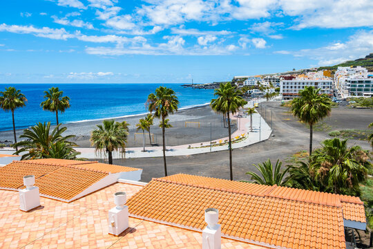 Elevated view of a coastal resort beach with black sand, palm trees, and terracotta roofs in Puerto Naos, La Palma, Canary Islands, Spain