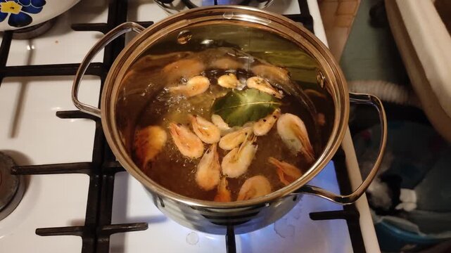 Cooking shrimp with bay leaf in stainless steel pot on gas stove, top view