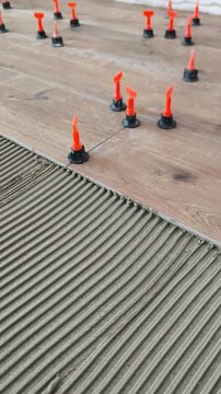 Notched-trowel tile adhesive on the floor and orange tile leveling systems.