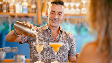 Smiling bartender preparing and serving refreshing summer drinks from a cocktail shaker at an outdoor bar © DMegias