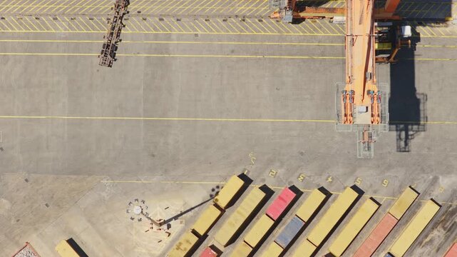 Terminal tractor maneuvering a semi-trailer chassis across a paved container yard. With rows of shipping containers and the shadow of a large gantry crane visible from a top-down aerial perspective