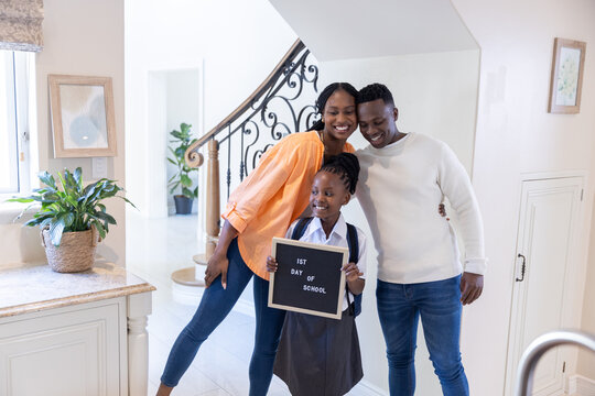 African American family posing in foyer, schoolgirl in grey uniform holding 1ST DAY OF SCHOOL sign