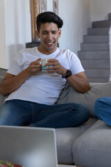 African American man with companion wearing white tee at home holding mug squinting at laptop © wavebreak3