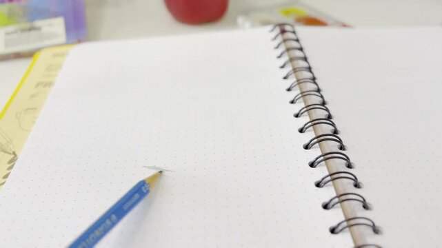 Close up of a blue pencil drawing a hatch pattern on the white dotted page of a spiral notebook, symbolizing creativity, artistic expression, and the beginning of a new idea