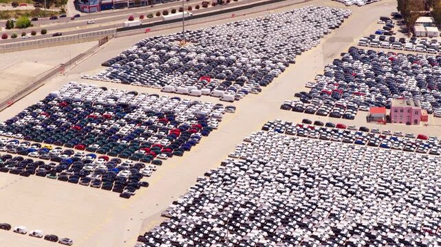High-angle perspective showing thousands of brand-new cars perfectly parked in a massive lot at a shipping port, all prepared for export and distribution through the global supply chain