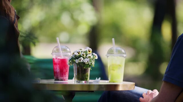Brightly colored cold beverages displayed on an outdoor cafe table with decorative flowers and soft focus greenery in the background