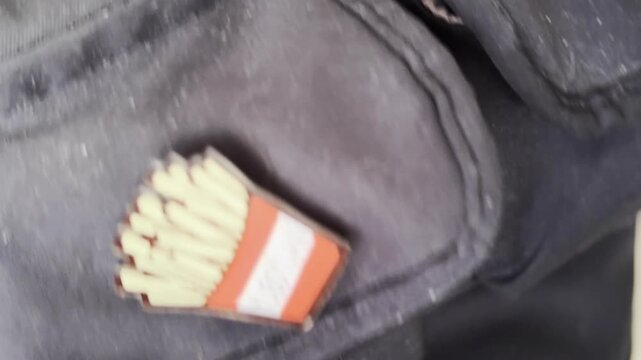 Woman's hand placing a smartphone into a backpack, revealing shoplifting of fries shaped eraser from a pocket in a humorous twist at the end of the shot