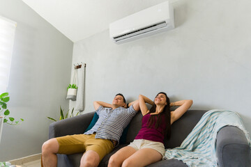 Obraz premium Happy couple relaxing at home enjoying cooling air from modern air conditioner during hot summer day