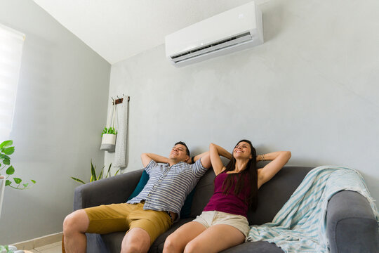 Happy couple relaxing at home enjoying cooling air from modern air conditioner during hot summer day