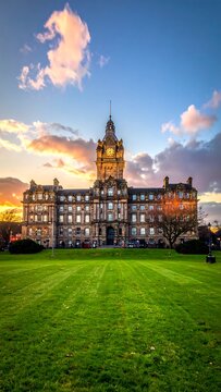 A blurry image of a large, old building with a clock tower on a grassy field at sunset