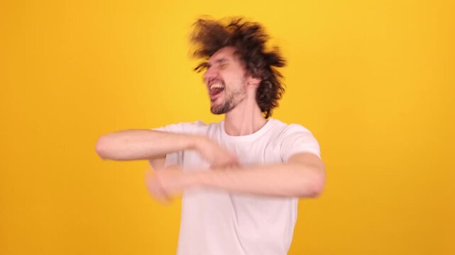 Joyful young person performing an energetic victory‑dance gesture in a bright yellow studio portrait, expressing excitement, movement and positive lifestyle emotion.