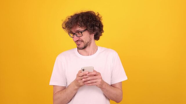 Person happily looking at a smartphone with a joyful expression, as if enjoying content, creating a bright upbeat mood in a vivid yellow studio portrait.