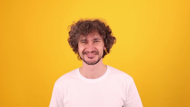 Person smiling and giving a playful wink in a bright yellow studio portrait, creating a friendly upbeat mood.