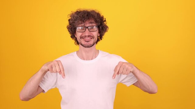 Young person pointing down with both index fingers in a bright yellow studio portrait, creating a clear attention‑directing gesture with a confident expressive pose.