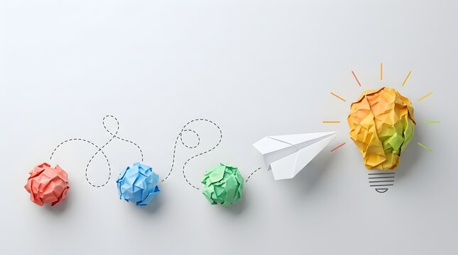 Creative process and journey to success concept with erratic path of crumpled paper balls leading to paper airplane and crumpled paper lightbulb with copy space