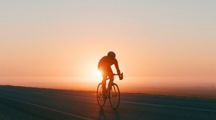 Obraz premium Cyclist riding along open road at sunrise, silhouette against bright sun, with clear sky and distant horizon visible in the background