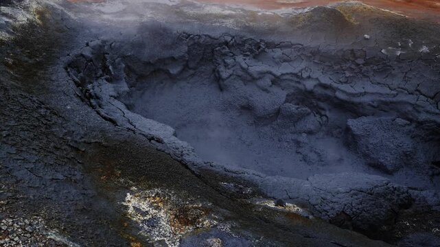 Bubbling Volcanic Mud Pool Emitting Steam in a Geothermal Area with Cracked Earth and Orange Hues