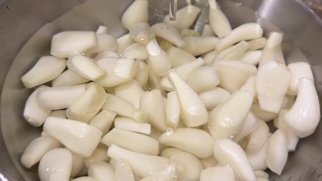 白い宝石と呼ばれるらっきょう。食用。らっきょうを洗うためにボウルに水を注いでるクローズアップ動画。