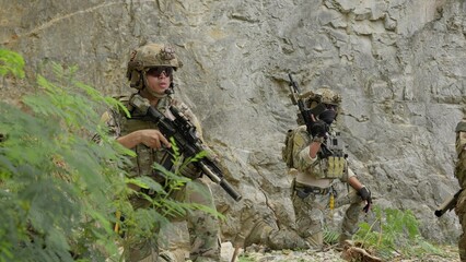 Obraz premium Special forces soldiers on patrol cautiously advance through rocky terrain, conducting a covert reconnaissance mission with tactical gear and assault rifles.
