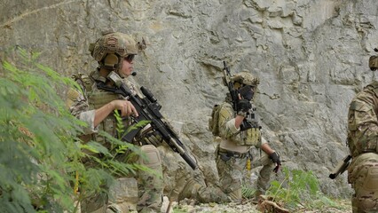 Obraz premium Special forces soldiers on patrol cautiously advance through rocky terrain, conducting a covert reconnaissance mission with tactical gear and assault rifles.