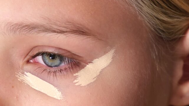 Close-up of concealer application under the eye using a cosmetic applicator. Beauty and skincare routine concept