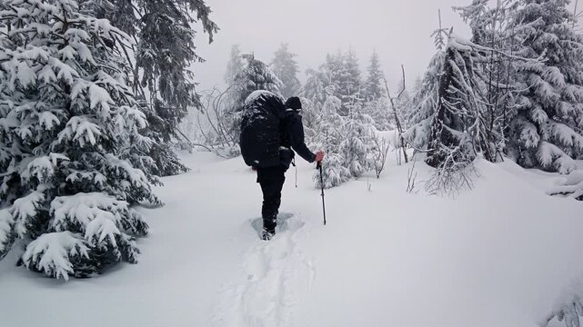 Hiker with backpack standing on snow covered mountain ridge during extreme cold weather