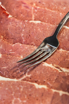 thin layered strips of cold cured macon meat on platter with silver serving fork at certified breakfast display.