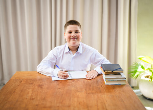 Smiling schoolboy sitting at a desk with notebook and books. Happy student studying at home or school. Education, learning, childhood development and academic success concept.