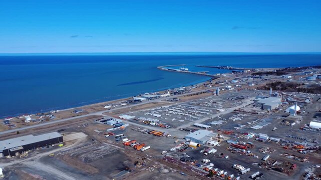 Aerial drone view of Matane's industrial waterfront featuring factories, warehouses, port facilities and the St. Lawrence River under clear skies.
