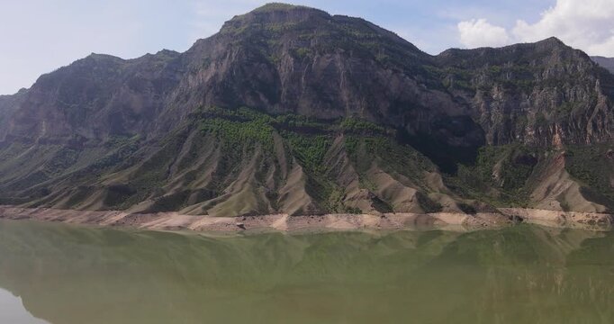 Epic aerial drone boom up shot of high mountain cliffs reflecting in the calm emerald water of Irganai reservoir in Dagestan