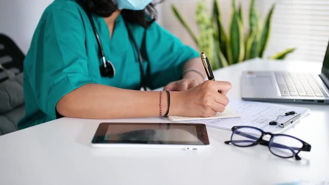 Medical personnel, nurses or doctors write medical notes in notebooks on their desks, looking busy.
