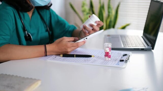 An Asian female doctor or pharmacist holds a medicine bottle and a smartphone tablet. Doctors providing online medication consultations.