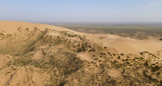 Cinematic aerial pull out shot of Sarykum sand dune ridge with wooden observation deck and distant valley in Dagestan