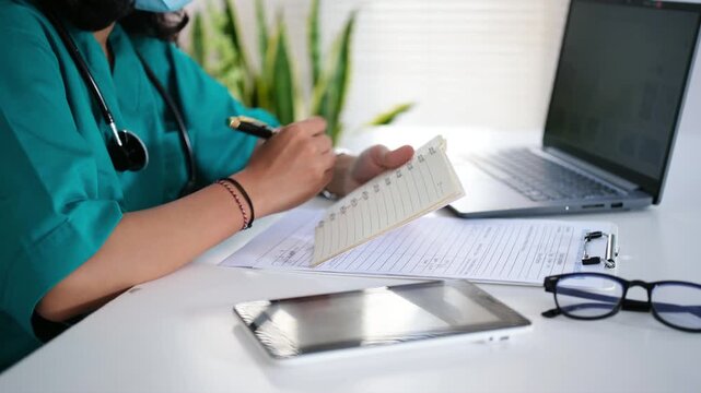 Medical personnel, nurses or doctors write medical notes in notebooks on their desks, looking busy.